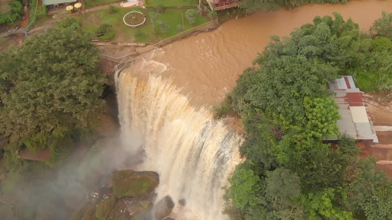 tiro giratorio aéreo alto de una enorme cascada que se estrella en el campo de vietnam rodeado de jungla verde
