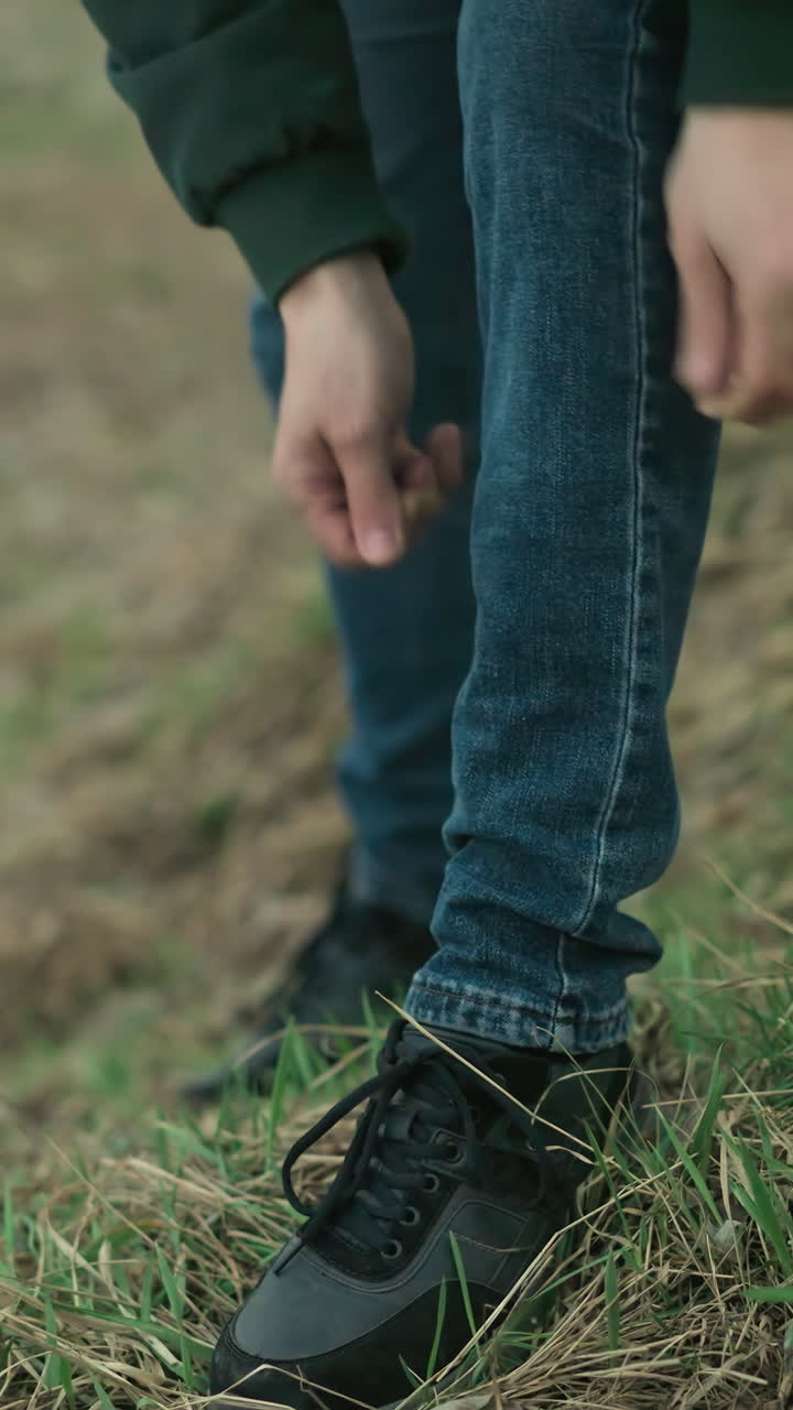 A close view of a man rolling down his jean trouser leg after inspecting his lower leg in an outdoor setting with a natural background of grass and earth