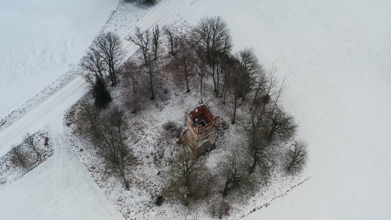 vista aérea del campo nevado y las ruinas del campanario de la antigua iglesia entre los árboles