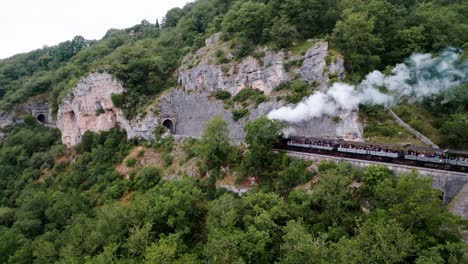 Drohnenverfolgung-Eines-Dampfzuges-Auf-Den-Gleisen,-Der-Auf-Dem-Weg-Durch-Einen-Tunnel-Zum-Bahnhof-In-Martel,-Einem-Dorf-In-Der-Region-Lot-In-Frankreich,-Fährt