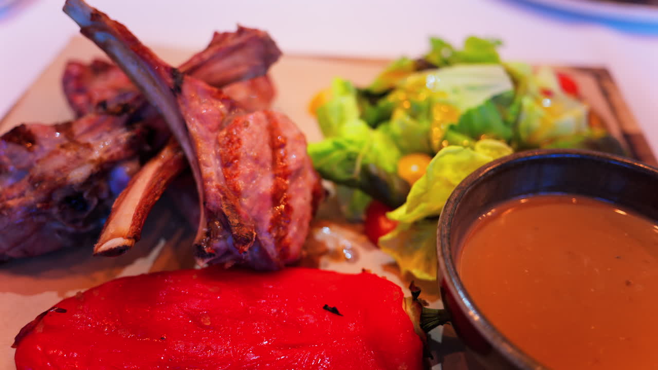 Close up of lamb chops with sauce and a side salad on a plate at a restaurant