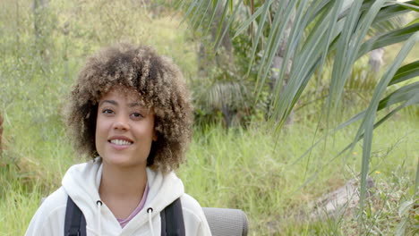 a young biracial woman with curly hair smiles in a natural outdoor setting with copy space