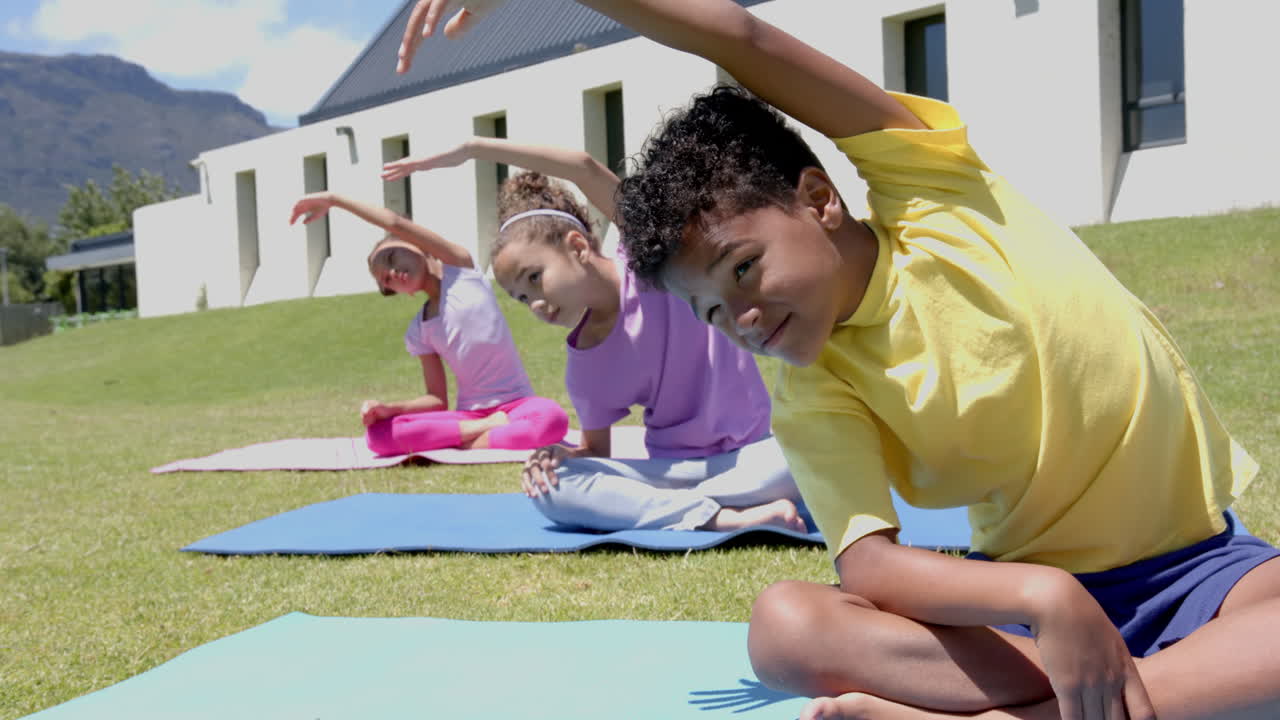 Biracial children do yoga outside on a sunny day, mountains behind, at school