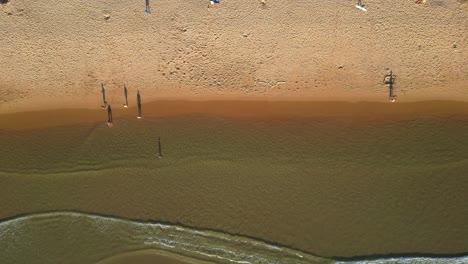 bird's eye view of people by the sea with the waves breaking and their magnificent shadow, some people running, others walking and others doing gymnastics.portugal