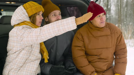 drie vrienden praten en wijzen iets terwijl ze op een besneeuwde winterdag in de kofferbak zitten