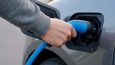 hand plugging a blue charger into a modern electric vehicle port