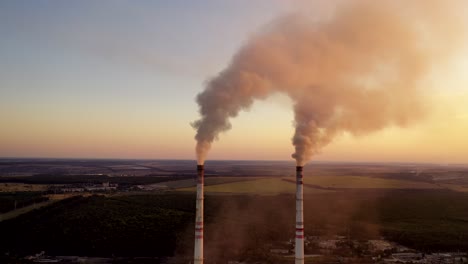 Industrial pipes with smoke. Metallurgical factory among green fields and forests in the evening. Aerial view.