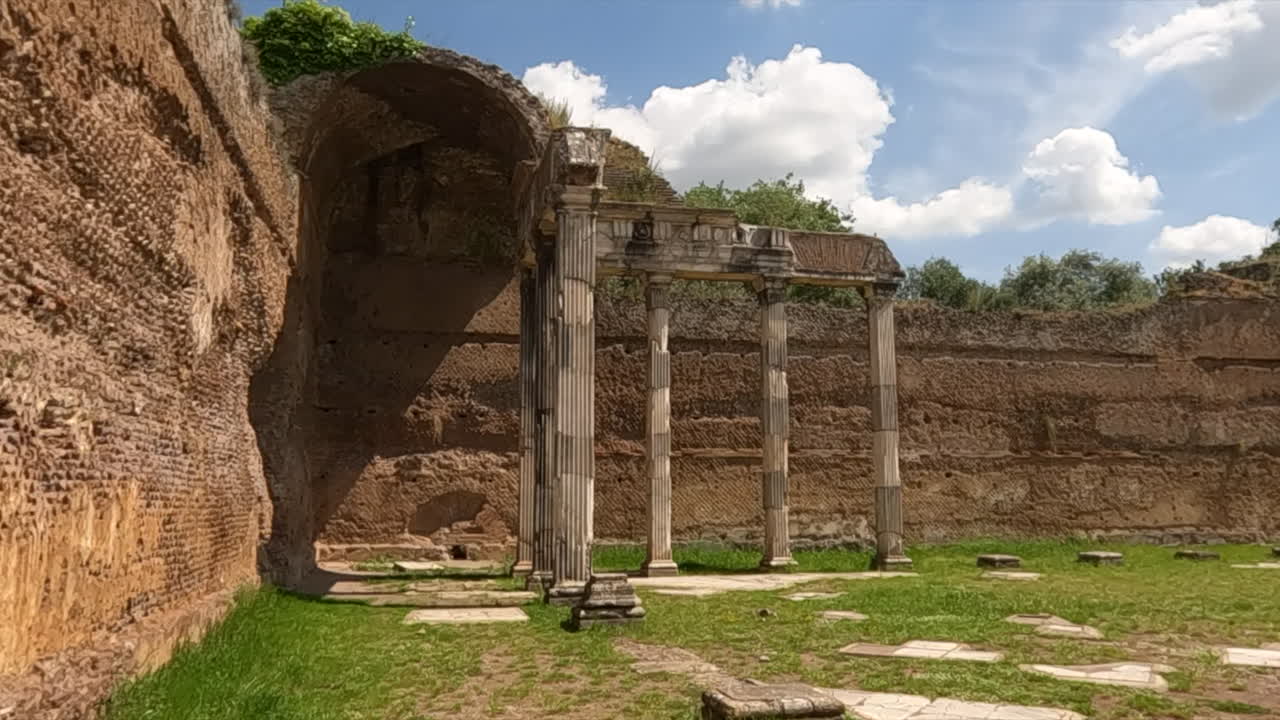Antiche rovine romane con colonne in piedi, un arco in pietra e erba verde lussureggiante sotto un cielo blu a Roma, Italia
