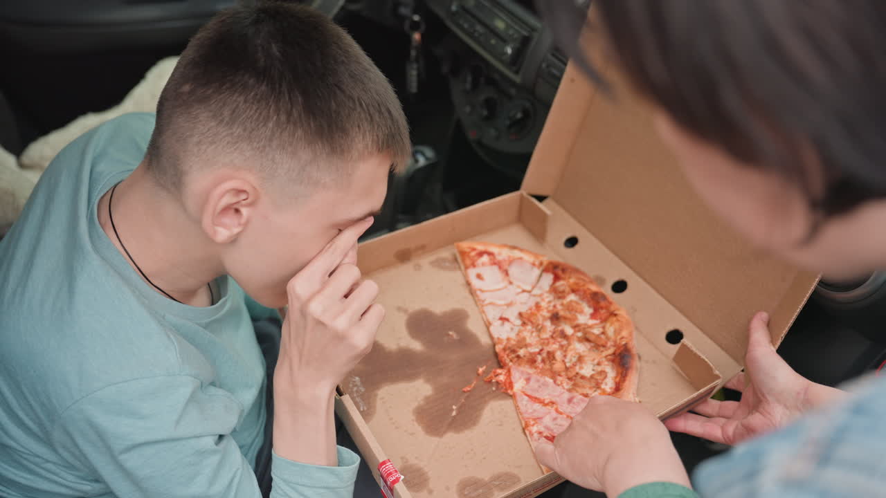 Teen Opening Greasy Pizza Box In Car, Caregiver Offering Slice And Steadying Box Close Intimate Scene With Stained Cardboard, Pepperoni Slice, Supportive Hands, Quiet Roadside Pause, Soft Natural