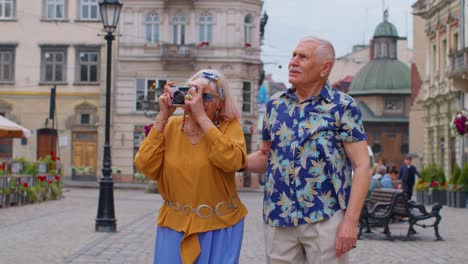 Senior-old-stylish-tourists-man-woman-walking,-taking-photos-on-old-camera-at-summer-city-center