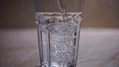 CLOSE-UP-SLOW-MOTION-Filling-a-transparent-glass-with-cold-water-from-a-glass-bottle,-on-a-laminate-surface-at-a-kitchen