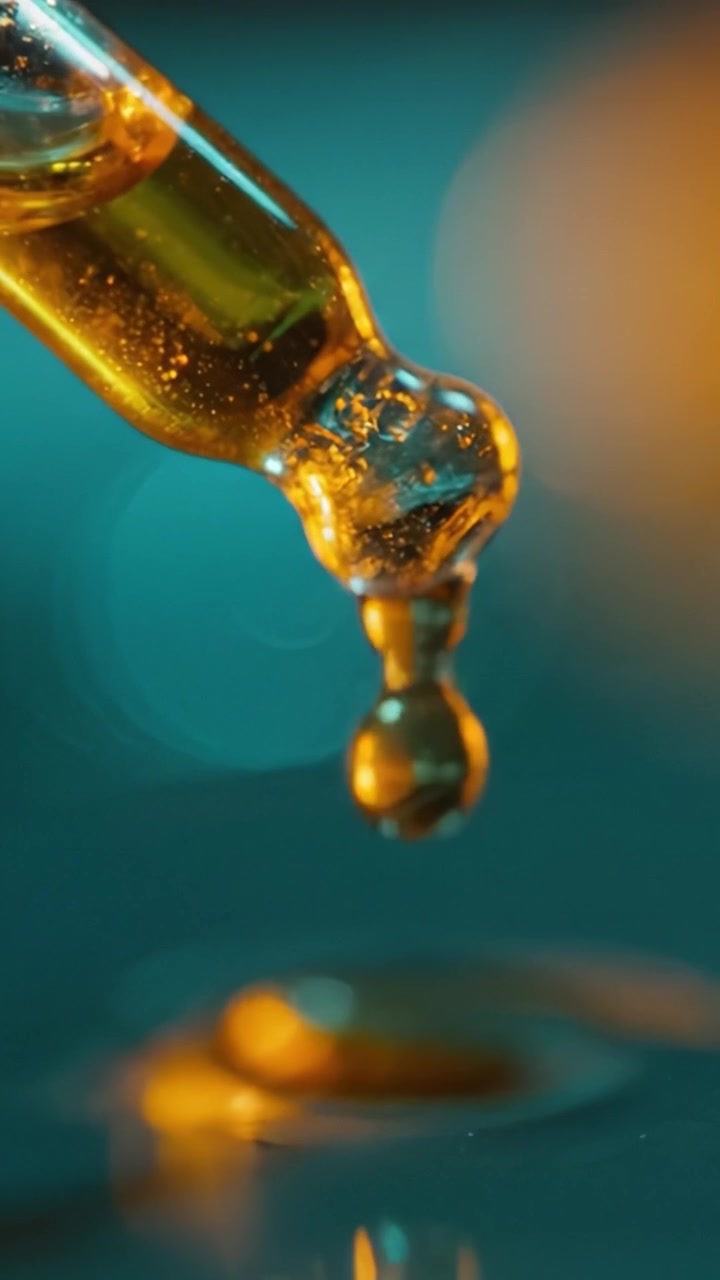 Close-Up of a Dropper with Golden Liquid Suspended Above a Surface, Highlighting Viscosity and Bubble Formation in a Macro Lens Perspective