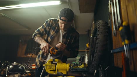 confident guy mechanic using a grinder grinds a part on a workbench in his workshop with many tools