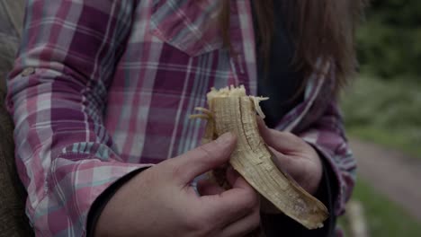 Frau-Sitzt-Auf-Einer-Bank-Auf-Dem-Land-Und-Isst-Eine-Banane