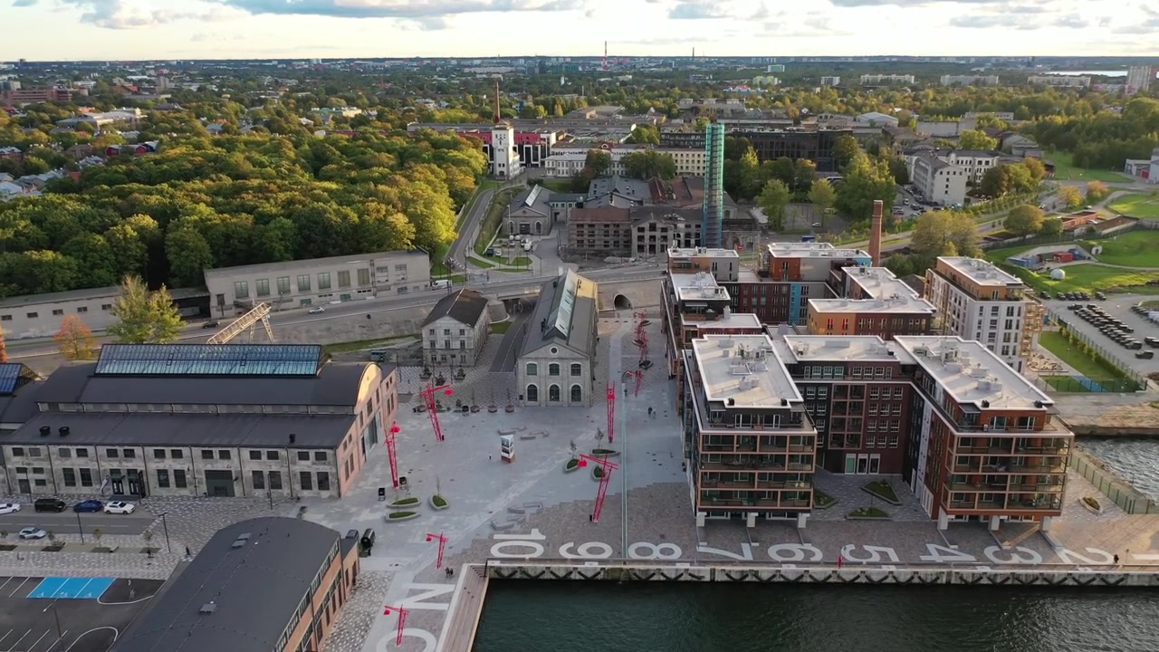 Vista aerea del quartiere Noblessner a Tallinn. L'inquadratura mostra cantieri navali storici in pietra convertiti accanto ad appartamenti di lusso moderni e lampioni di design rossi vicino al porto del Mar Baltico