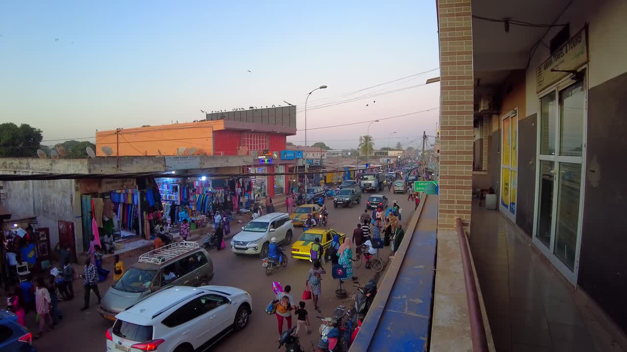 Dynamic pan high angle view of main Serekunda Market street traffic during sunset