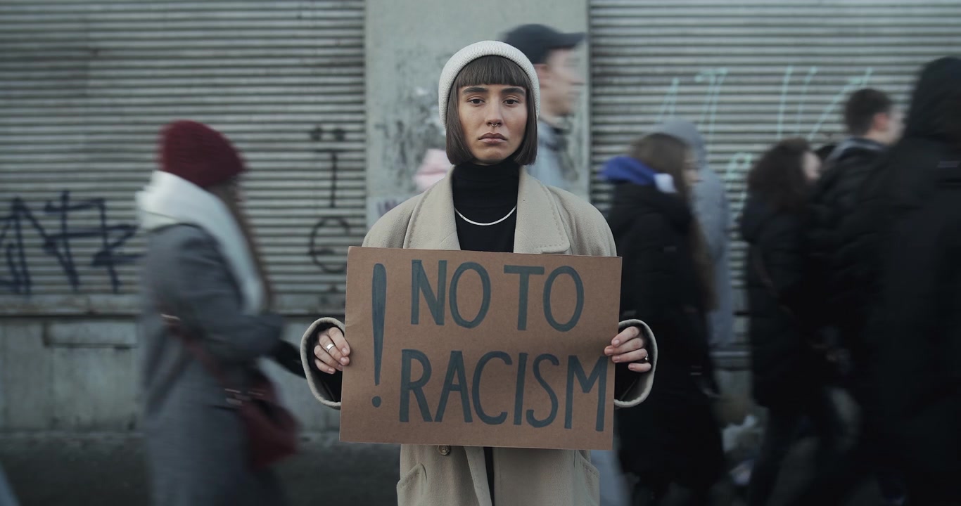 Young Woman Holding No To Racism Sign in Busy City Street