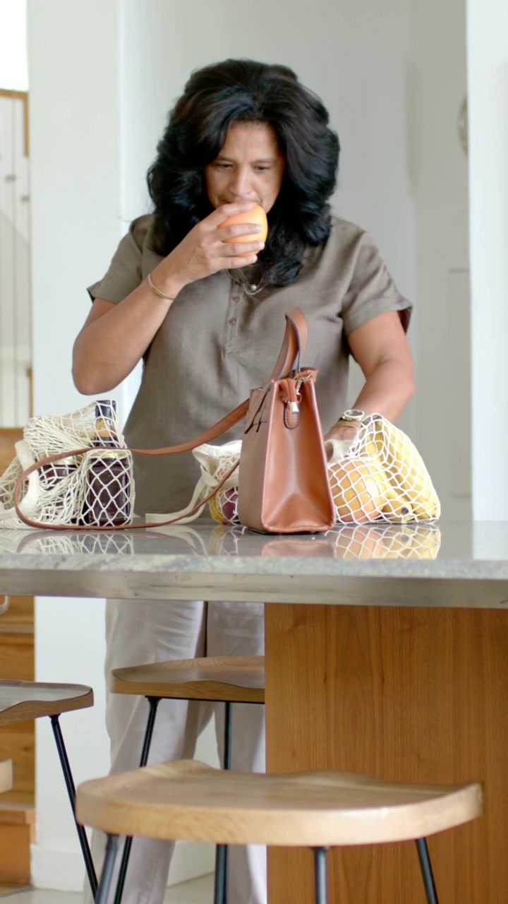 Video verticale: Donna in top che tiene un agrume, controlla se è maturo, lo annusa e lo posiziona vicino a delle borse in cucina.