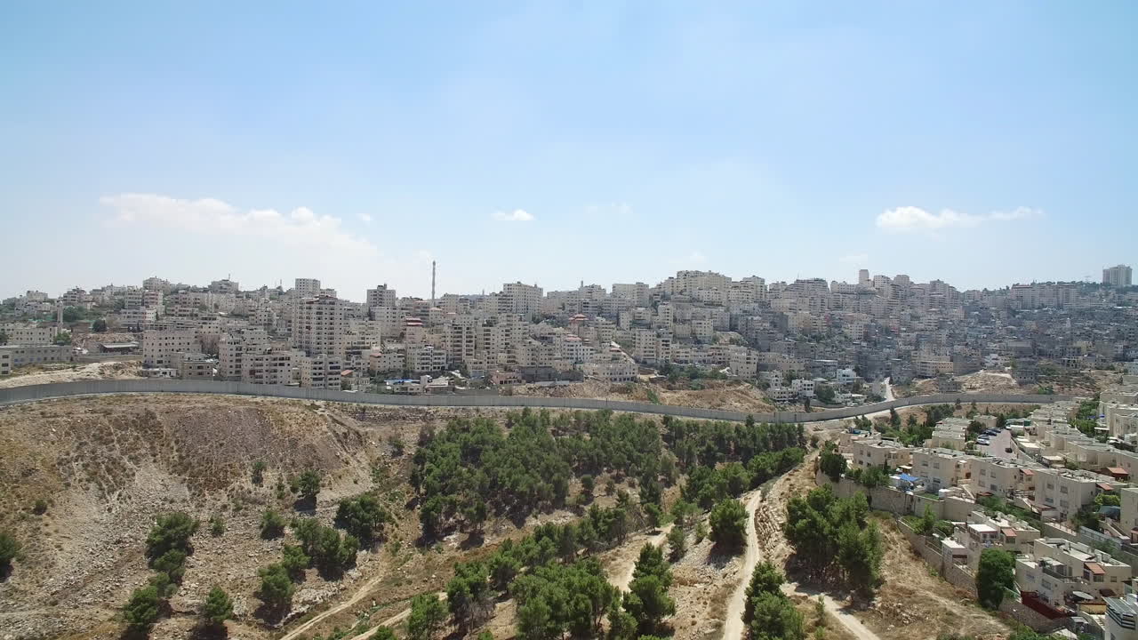 Panoramic view of a cityscape with a barrier wall and arid valley below