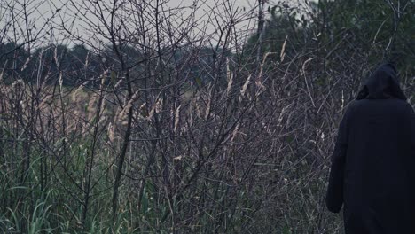 back view of a dark figure outdoors. ghost in black cloak going away on nature evening background.