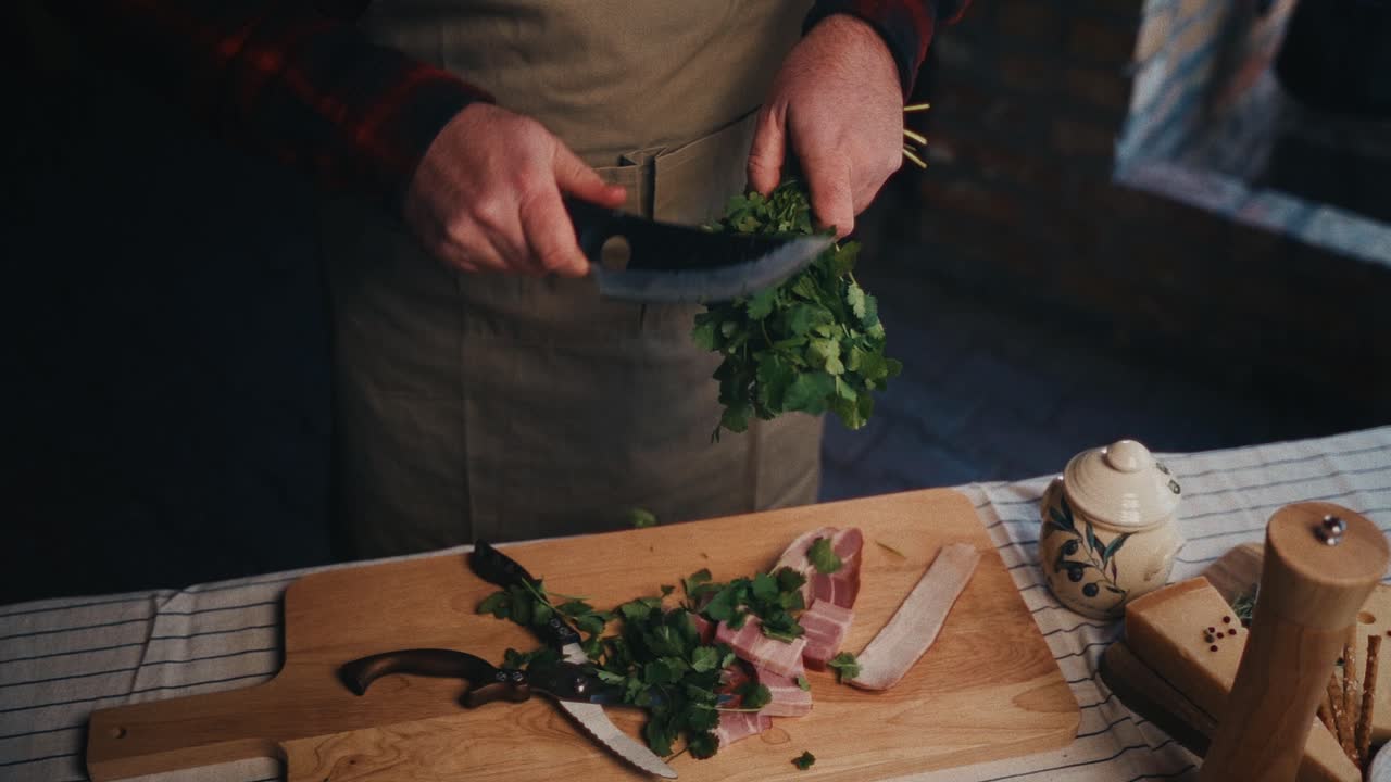 una persona corta hierbas frescas en una tabla de madera con tocino y utensilios de cocina cerca
