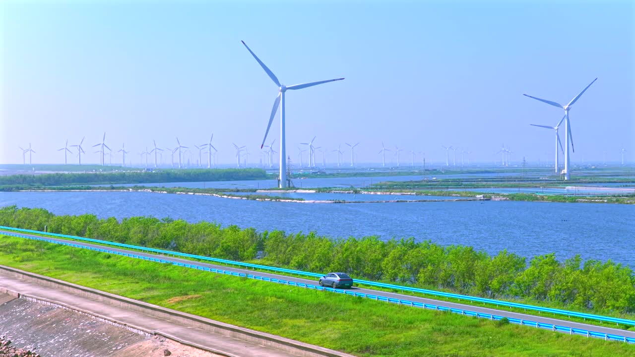 An electric car is driving outdoors, with a spinning windmill in the distance. Green new energy vehicle video