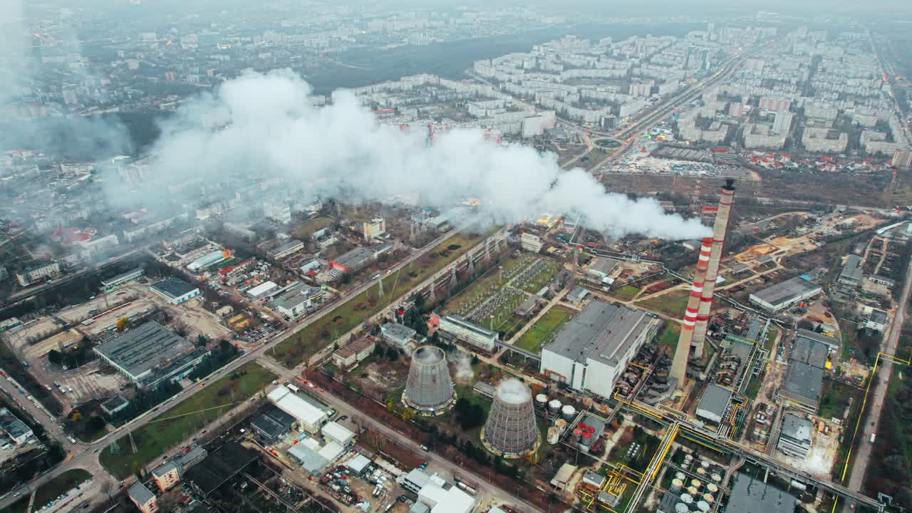 Aerial drone view of thermal power plant in Chisinau at cloudy weather, Moldova. View of pipes with felling steam, buildings and yellowed trees around