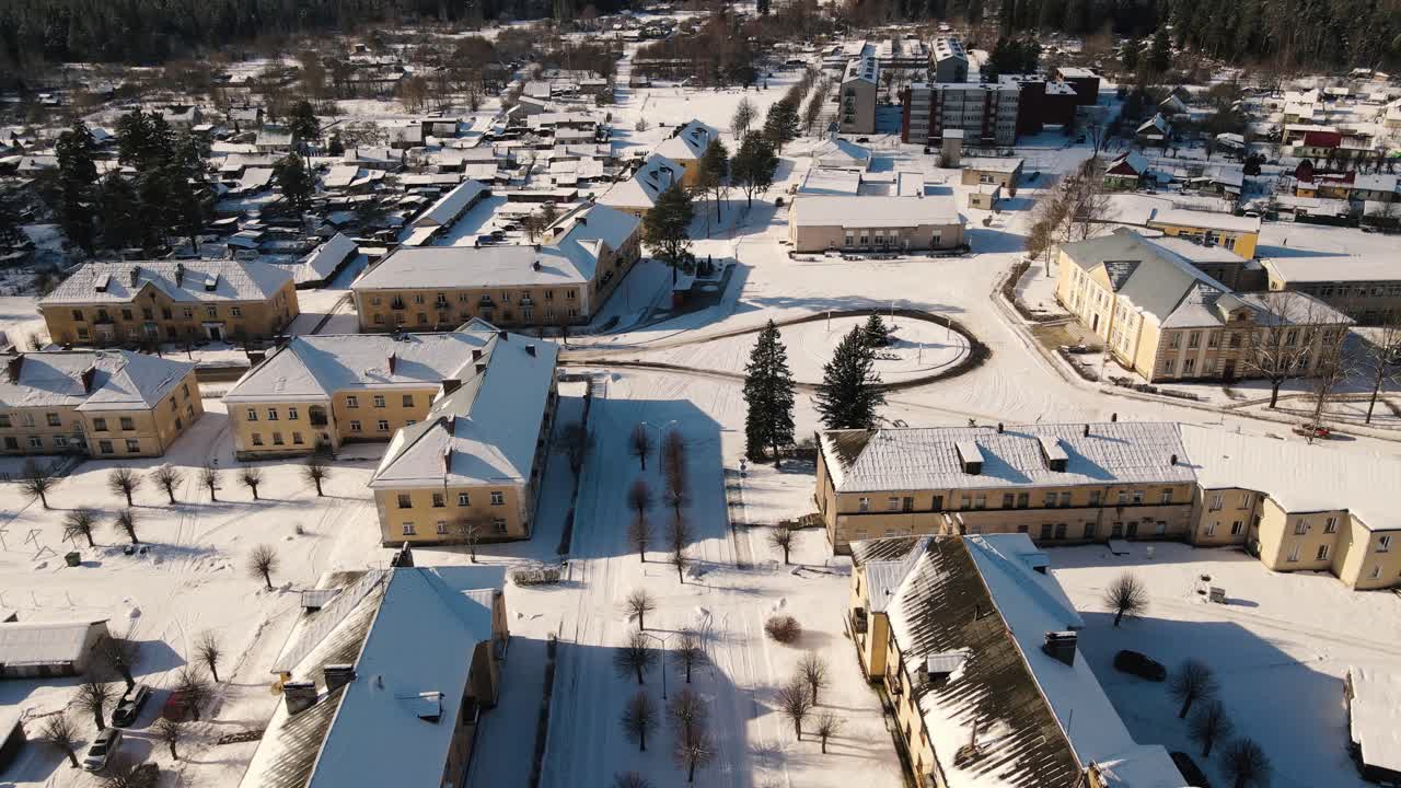 Aerial view of the snow-covered small town of Seda with yellow buildings, streets and roofs covered in white. A peaceful winter landscape in the sunlight.