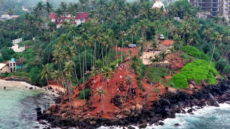 aerial elevated telephoto captures parrot rock, mirissa, sri lanka on an overcast day. visitors ascend the red-earth trail amid lush palms, dark rocks, and coastal views