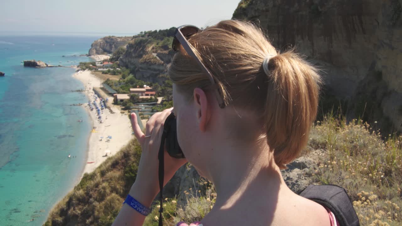 mujer en un acantilado está tomando fotos de la playa