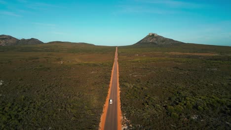 una foto aérea de una furgoneta conduciendo en una carretera recta en el parque nacional de cabo legrand en australia occidental con el pico francés en el fondo en un día soleado