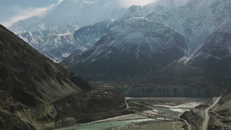 cinematic aerial view of hunza valley river with tilt up reveal of snow capped mountains