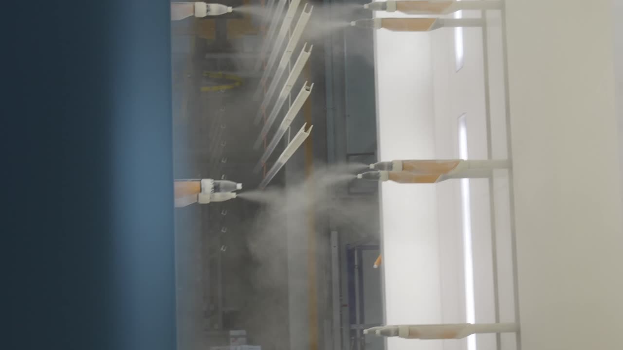Industrial powder coating booth applying fine powder layers onto suspended metal components. Continuous automated finishing workflow