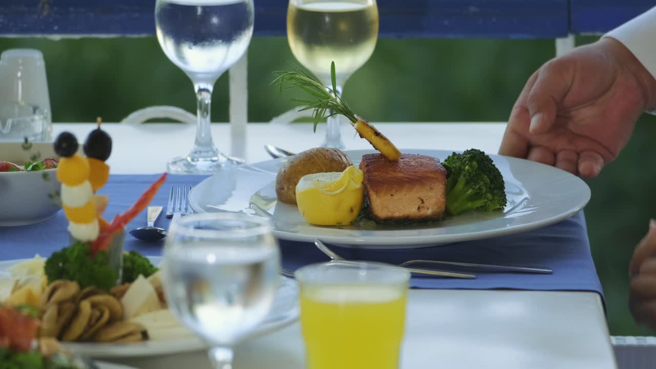 웨이터의 손이 가까이 있는 측면 보기는 레스토랑의 테이블에 음식 접시를 놓습니다.