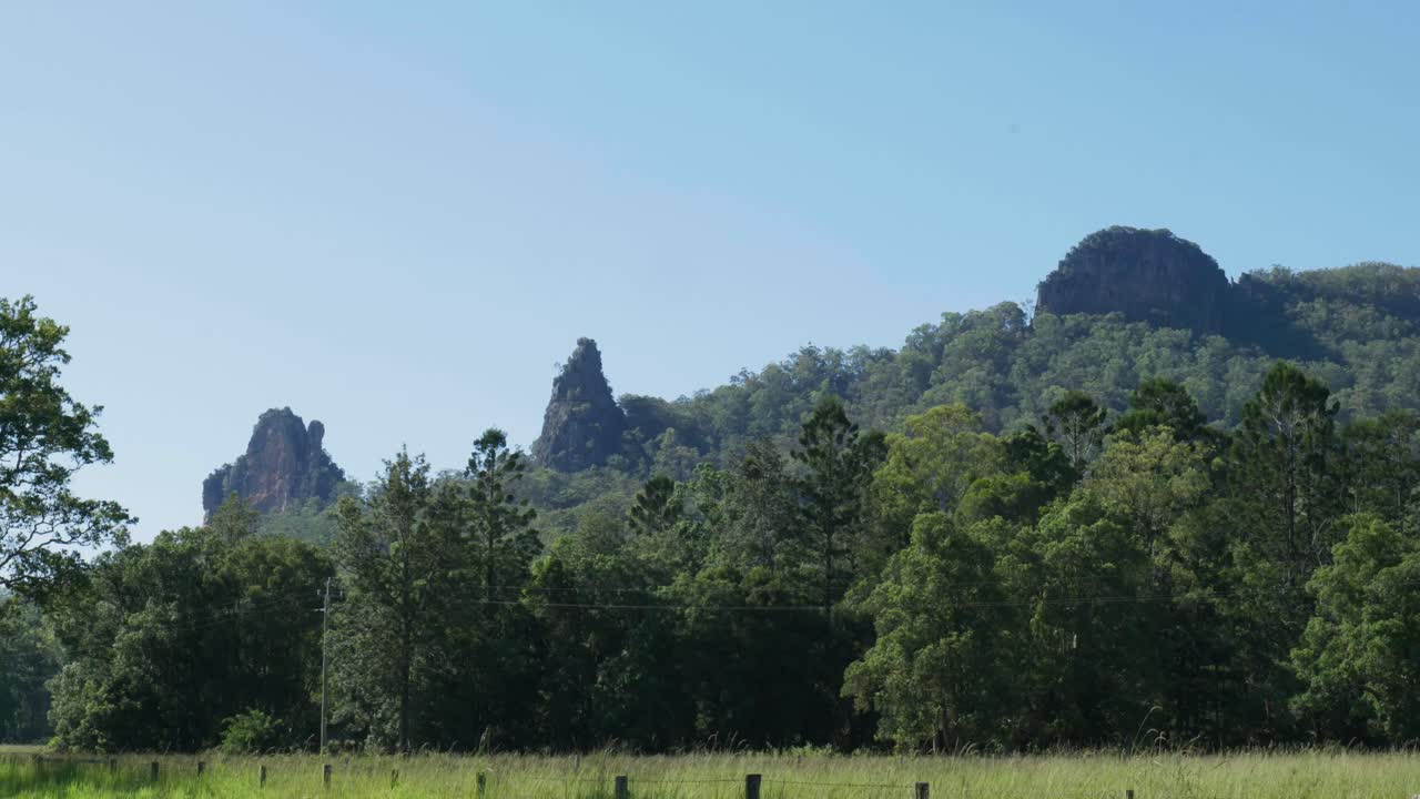 The Nimbin Rocks rise dramatically from the lush green landscape, showcasing ancient volcanic formations and vibrant natural beauty under a clear blue sky.