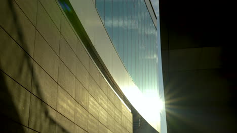 Sunlight-streaming-alongside-a-modern-building,-creating-a-play-of-light-and-shadow-on-its-stone-wall-and-reflective-glass