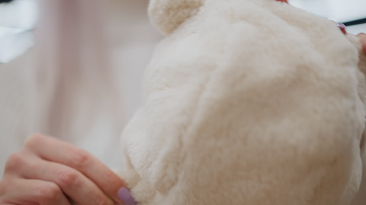 Hand view expectant mother feeling soft wool winter cloth in baby section of store, testing plush fabric texture, pastel garments blurred in background under warm lighting