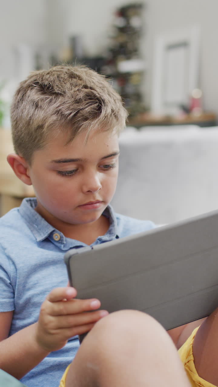 Vertical video of happy caucasian boy lying on sofa and using tablet, slow motion