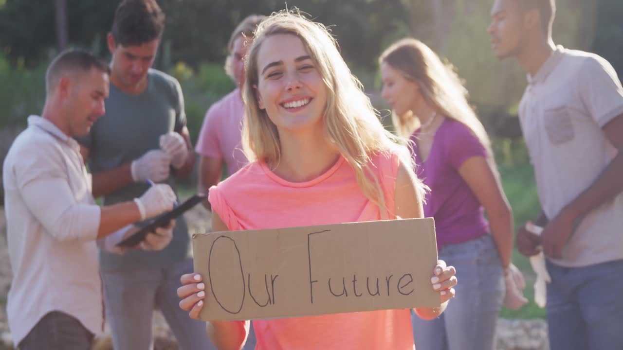 Un adulto che sorride e guarda in camera con una donna che tiene in mano un cartello con scritto "Il Nostro Futuro" durante una giornata di pulizia del fiume.