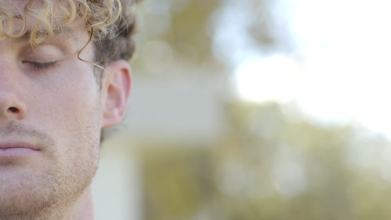 Luce solare che fa aprire l'occhio sinistro a un uomo adulto, sorridendo alla fotocamera all'aperto con effetto bokeh e spazio per il testo.