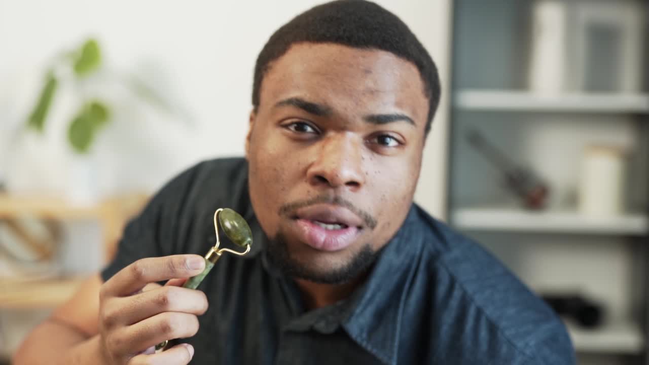 A dark-skinned guy massages his skin with a jade roller