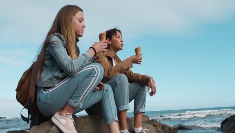 side view of a caucasian and a mixed race girl eating ice cream seaside