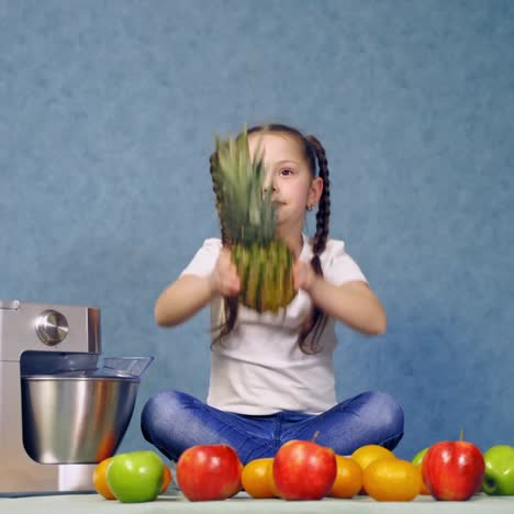 funny kid playing with pineapple. little girl is sitting on the table with many fresh fruits. new squeezer near organic food.