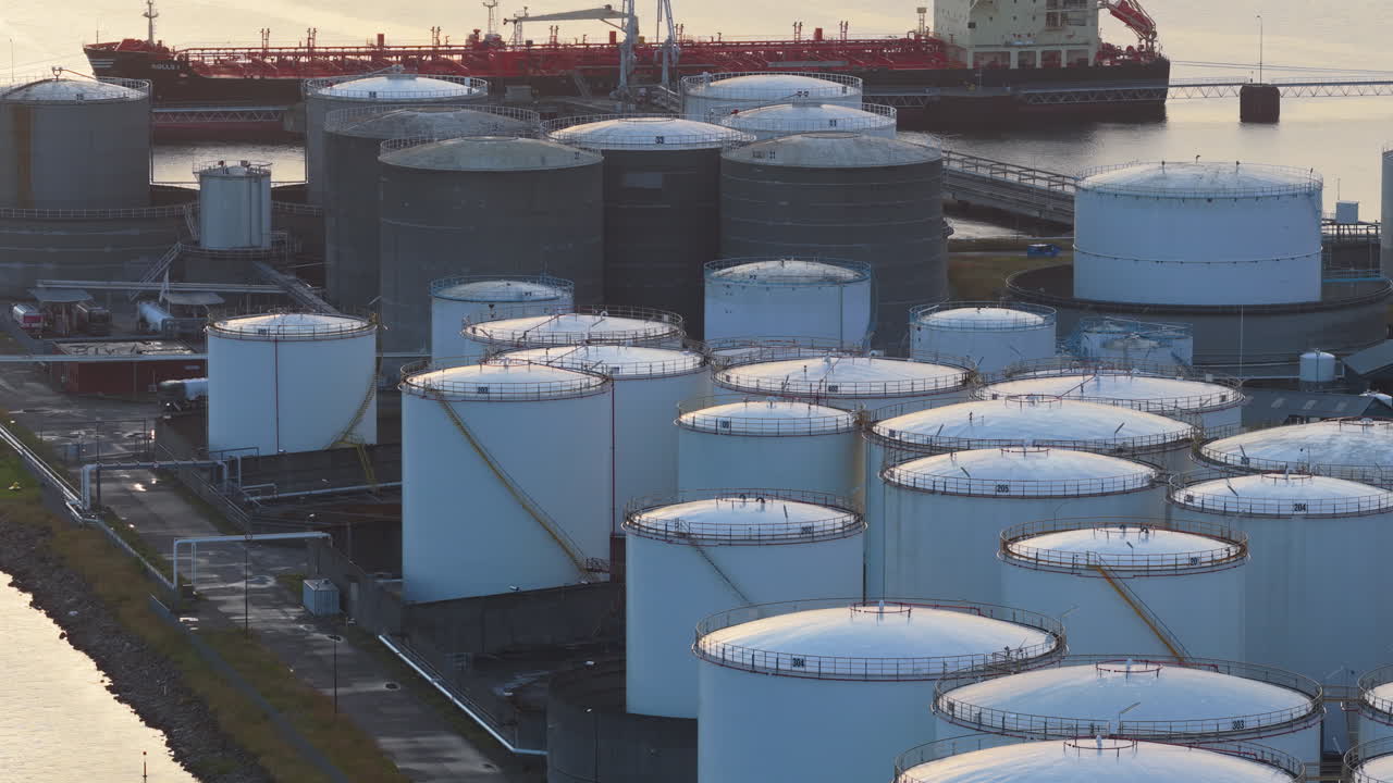Aerial drone view of large oil storage tanks in Copenhagen Harbor, Denmark, with offshore wind turbines and the sea in the background at sunset