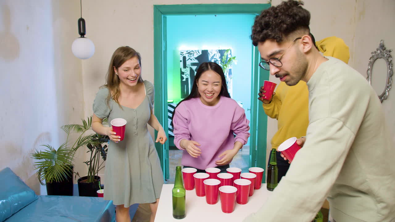 Happy multiethnic young friends playing beer pong at home