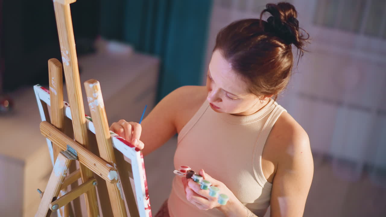 Woman Creating Art In Cozy Studio, Relaxed Woman Engaged In Painting In Warm Living Room Environment, Serene Female Artist Working On Canvas Amidst Gentle Glow In Comfortable Studio Setting