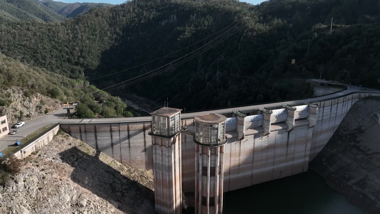 Luftfoto, der stiger op over Sau-reservoirets betonvandkraftdæmning i en grøn skovklædt dal.