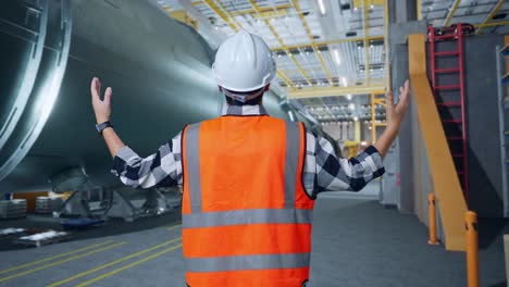 vista trasera de un ingeniero masculino asiático con casco de seguridad extendiendo los brazos mientras está de pie en una fábrica de fabricación de tubos