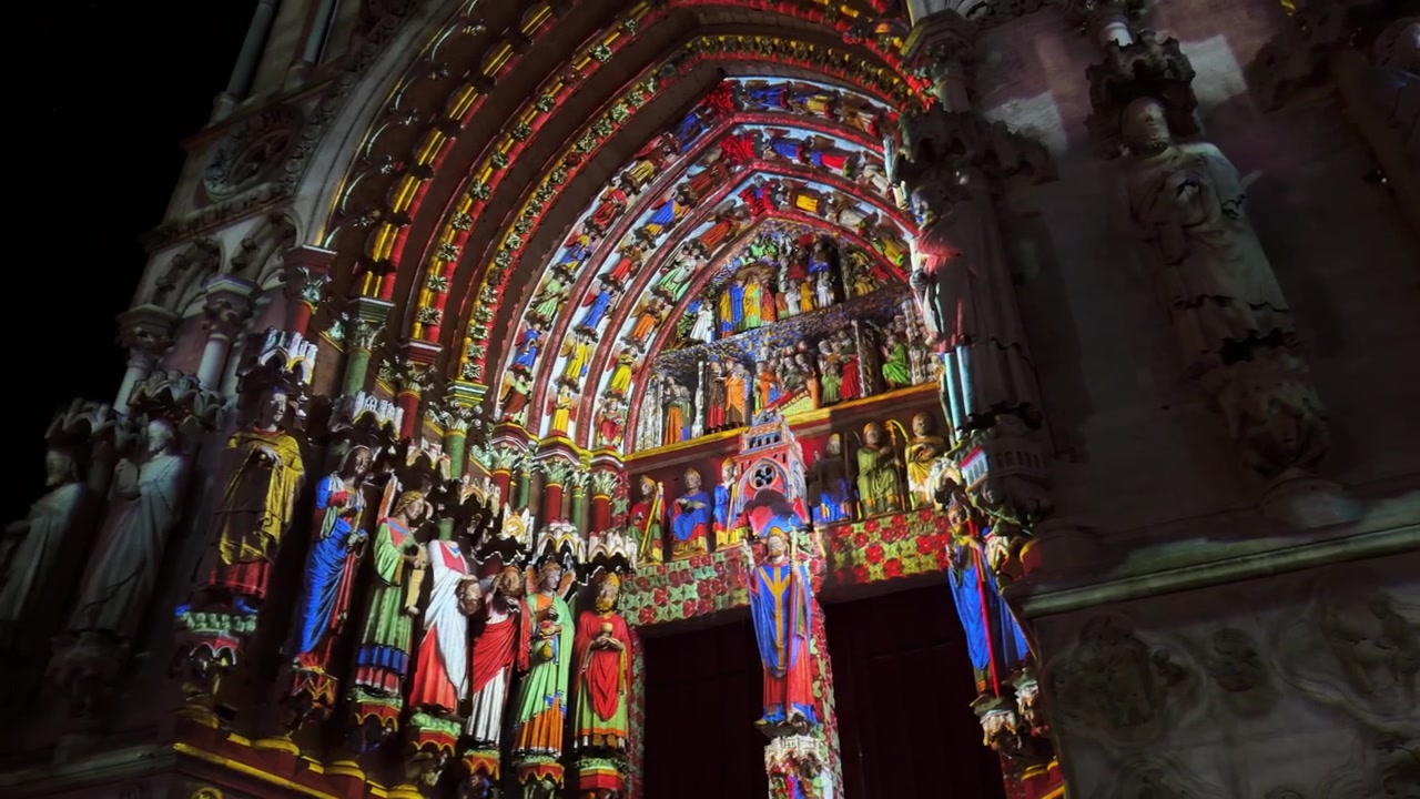 Proiezioni di luci colorate illuminano le statue e gli archi della facciata della cattedrale durante la notte