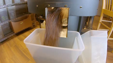 roasted coffee beans pouring from cooling tray into a plastic bin